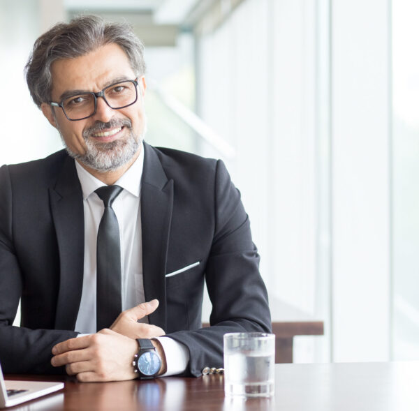 Cheerful businessman in eyeglasses working in office or coworking space. Portrait of confident male executive with gray hair at table. Successful business concept